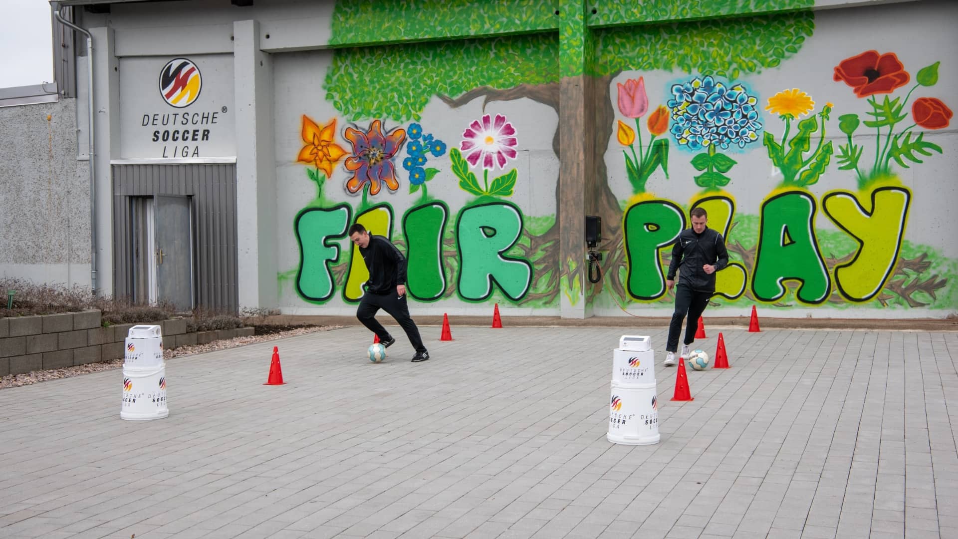 Zwei Personen bei einer Übung mit Sensortechnologie vor einer "FAIR PLAY"-Wand.